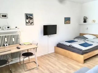 Minimalist bedroom with a neutral color palette, featuring a double bed and a simple desk setup with artwork on the walls